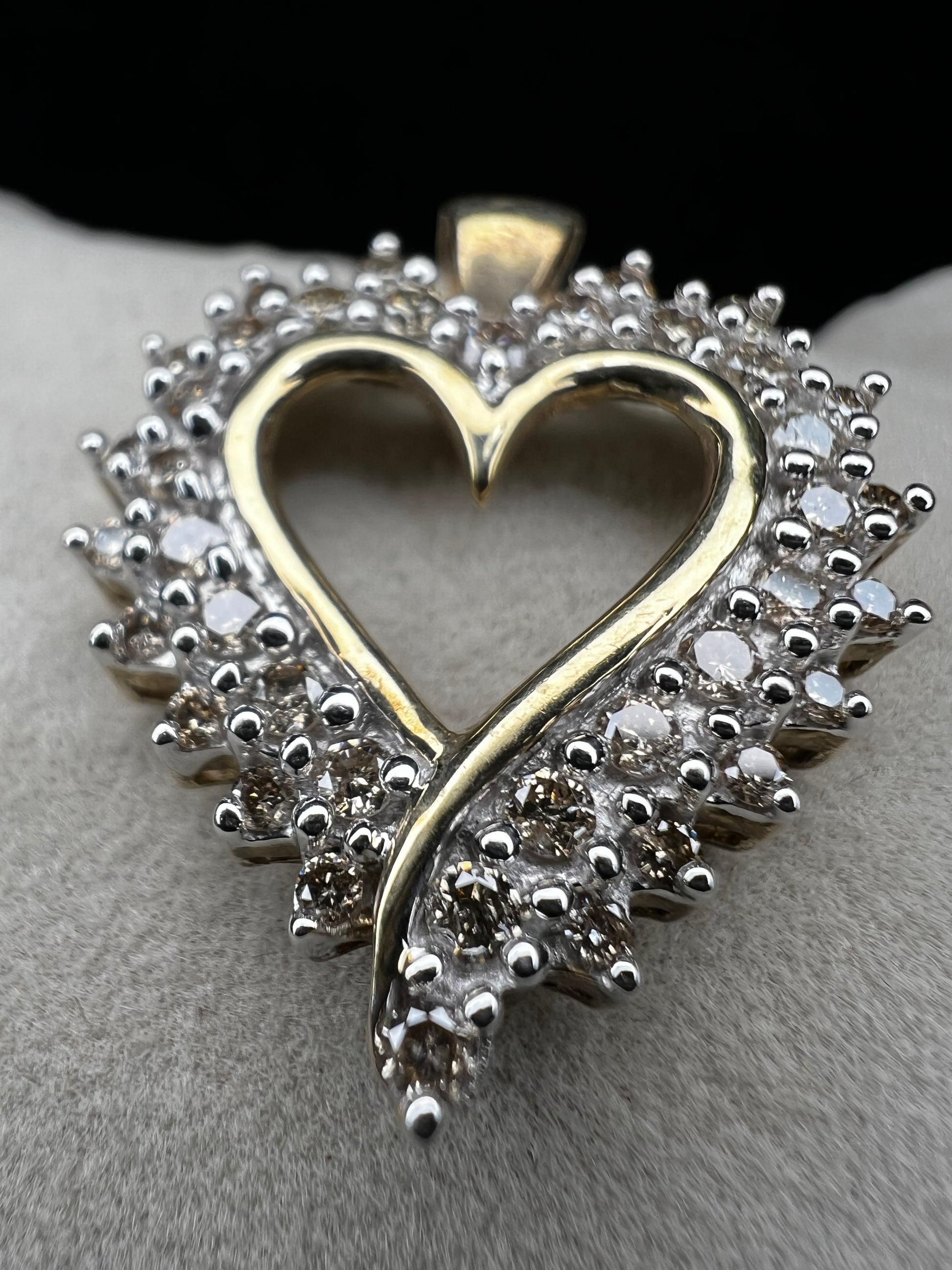 This heart-shaped pendant is crafted with 10 karat yellow gold with a bright white finish around the top to accentuate dazzling natural diamonds that cover the face of this piece.