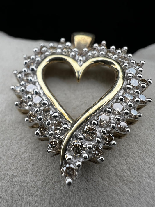 This heart-shaped pendant is crafted with 10 karat yellow gold with a bright white finish around the top to accentuate dazzling natural diamonds that cover the face of this piece.