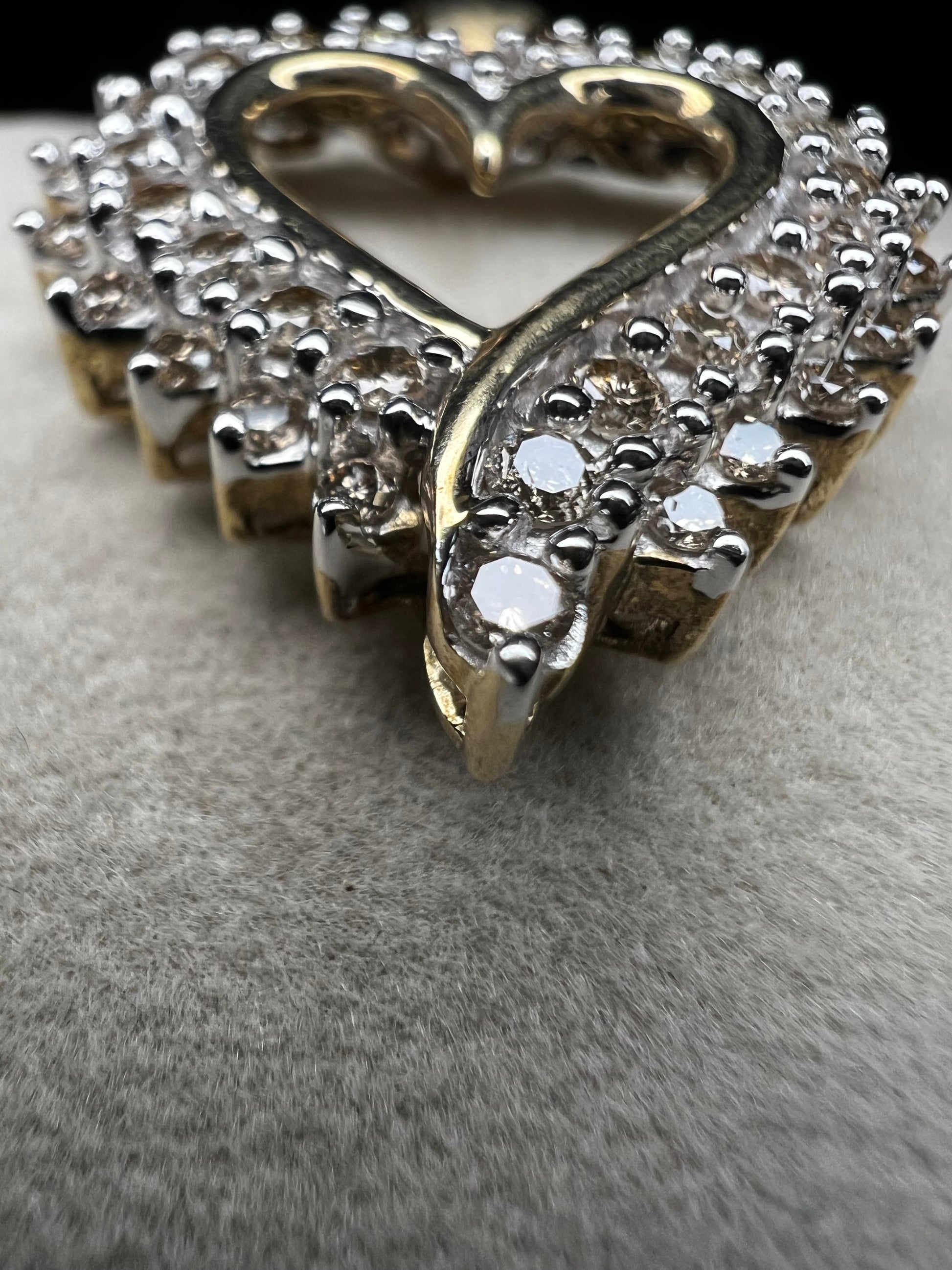 This heart-shaped pendant is crafted with 10 karat yellow gold with a bright white finish around the top to accentuate dazzling natural diamonds that cover the face of this piece.