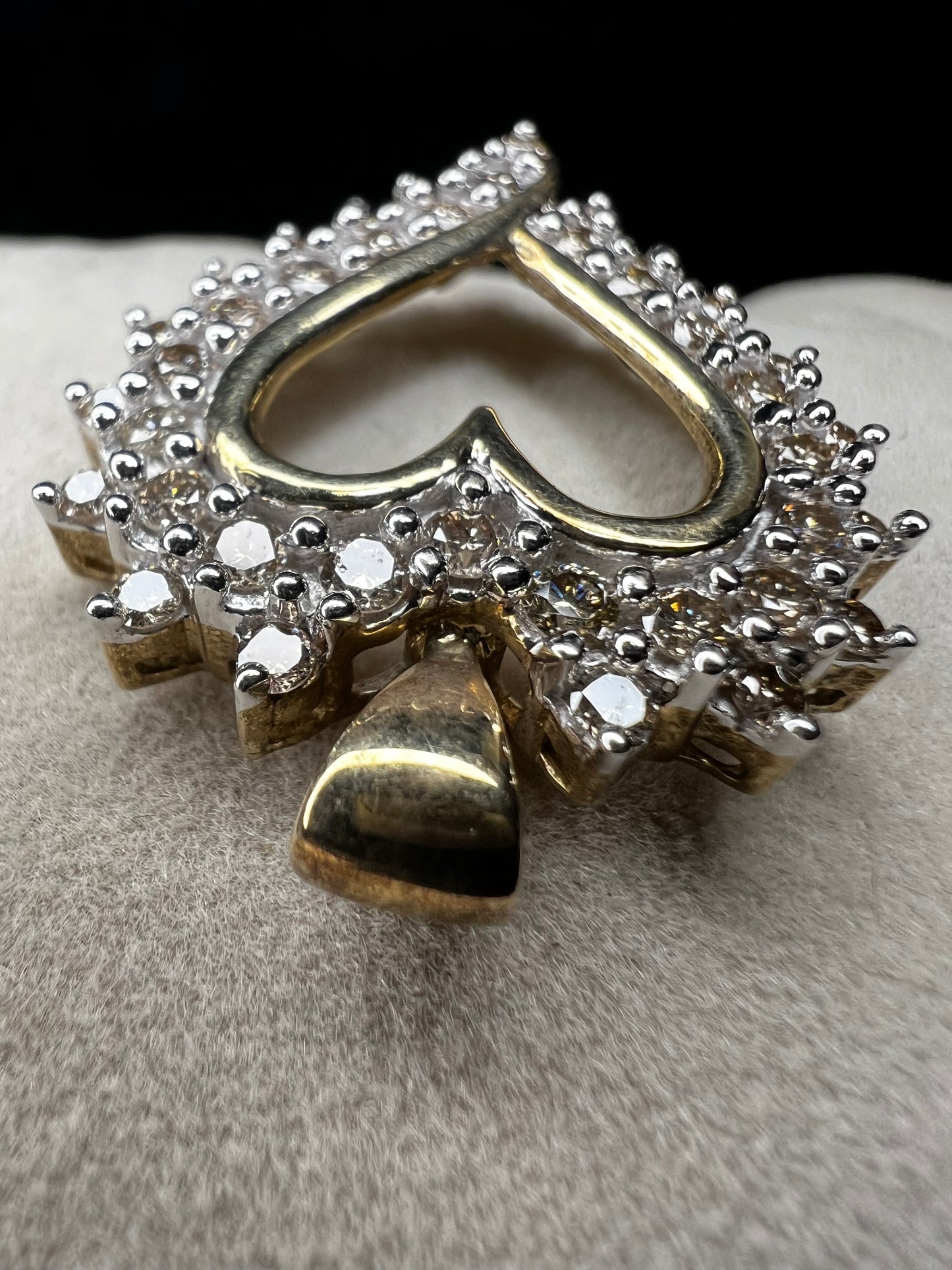 This heart-shaped pendant is crafted with 10 karat yellow gold with a bright white finish around the top to accentuate dazzling natural diamonds that cover the face of this piece.