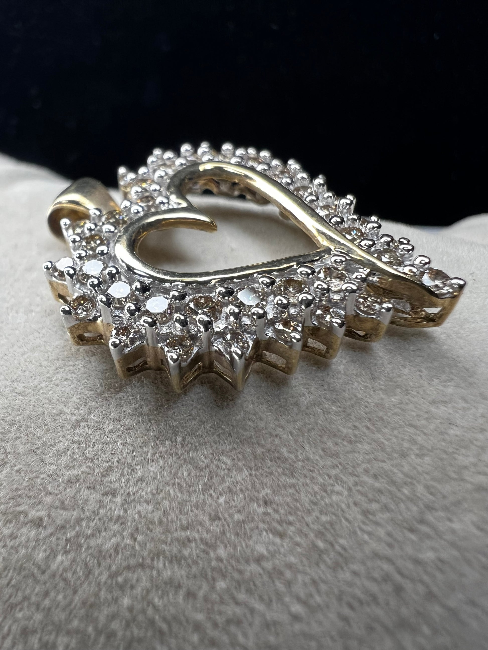 This heart-shaped pendant is crafted with 10 karat yellow gold with a bright white finish around the top to accentuate dazzling natural diamonds that cover the face of this piece.
