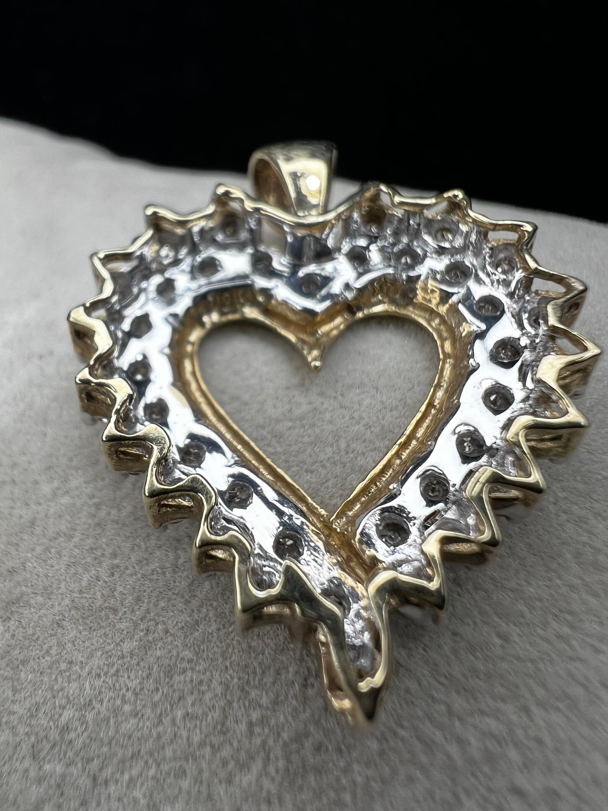 This heart-shaped pendant is crafted with 10 karat yellow gold with a bright white finish around the top to accentuate dazzling natural diamonds that cover the face of this piece.