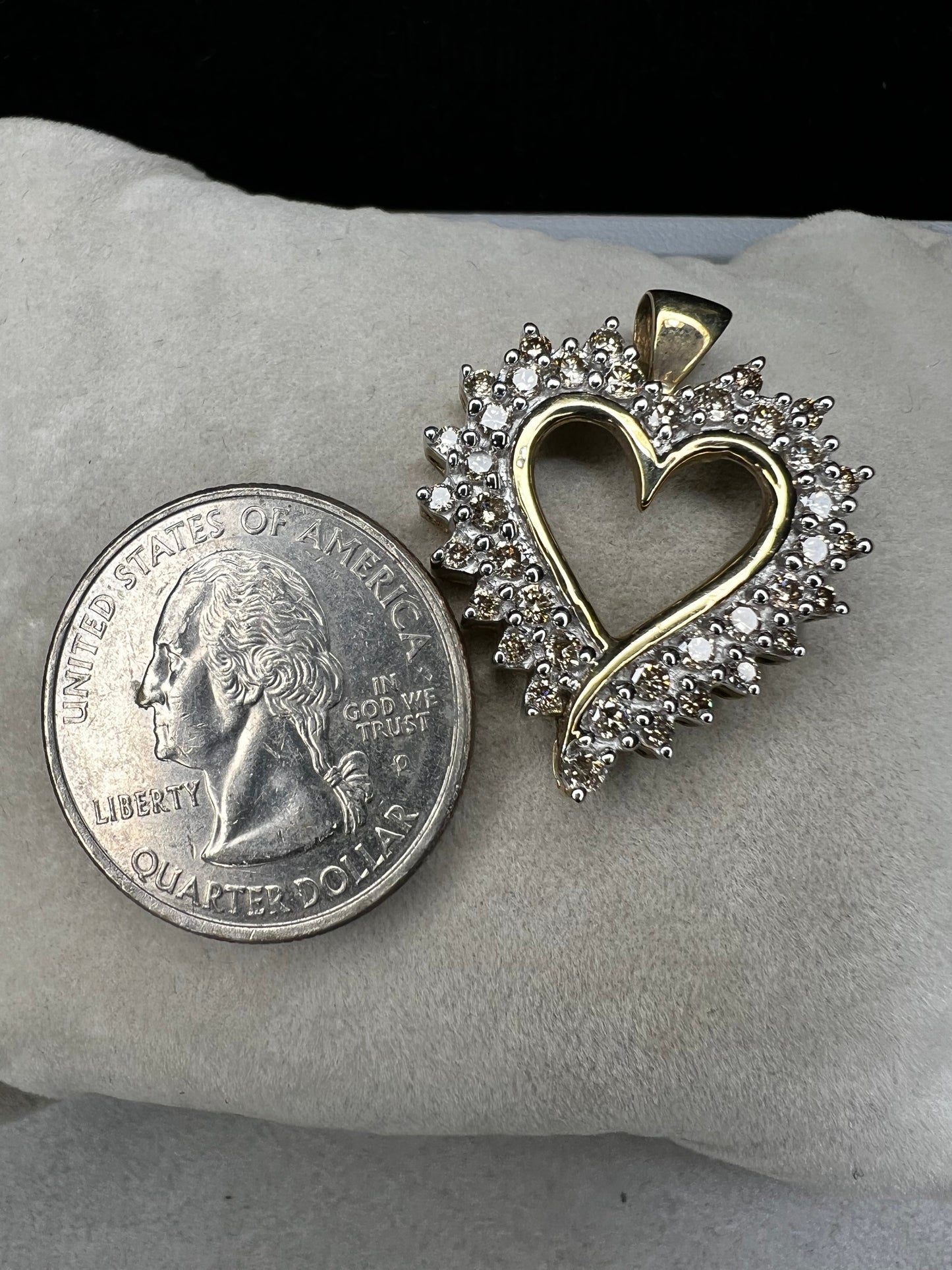 This heart-shaped pendant is crafted with 10 karat yellow gold with a bright white finish around the top to accentuate dazzling natural diamonds that cover the face of this piece.