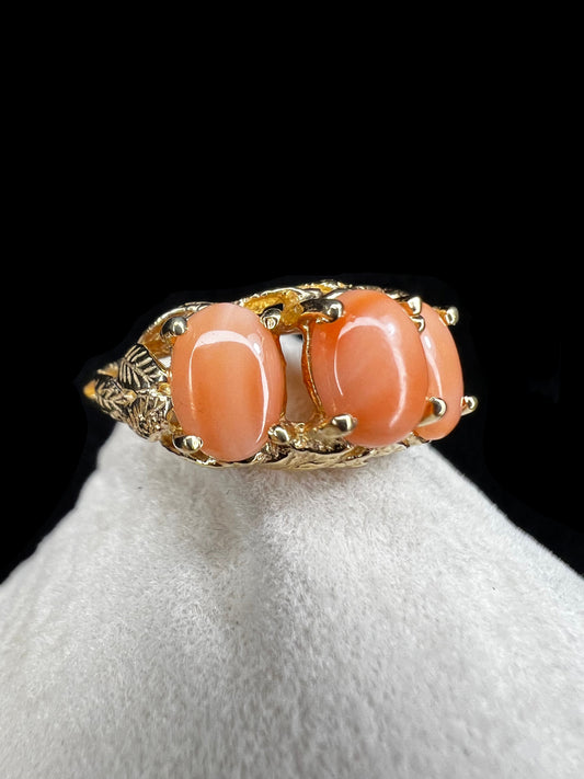 This exquisite ring, crafted in the Bahamas from 14 karat gold, features three peachy-salmon coral cabochons elegantly set amid intricately designed gold leaves. The combination of warm coral hues and detailed goldwork creates a distinctive piece.